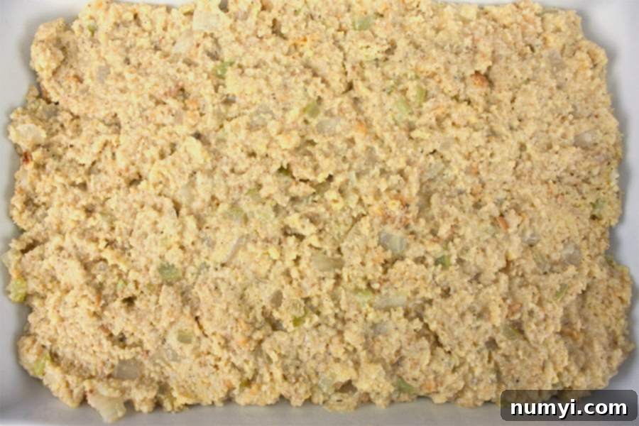Unbaked Southern cornbread dressing mixture evenly spread in a white ceramic casserole dish, ready for the oven.