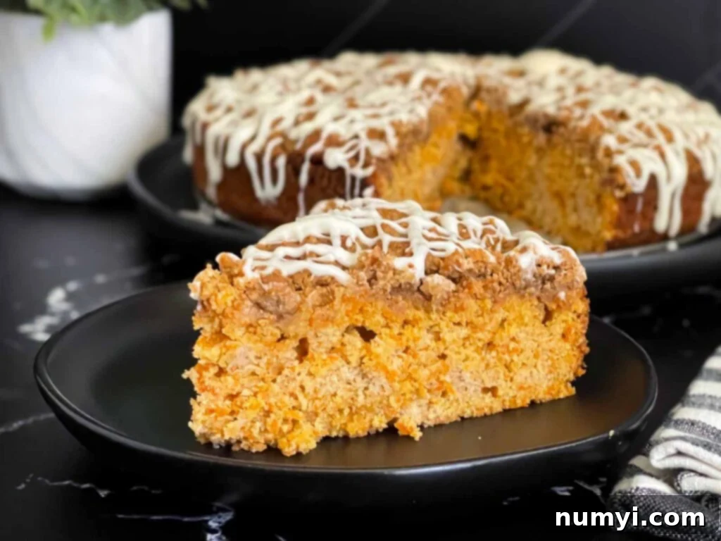 A perfectly sliced piece of carrot coffee cake on a dark plate, showcasing the fluffy interior, crunchy streusel, and delicate vanilla glaze.