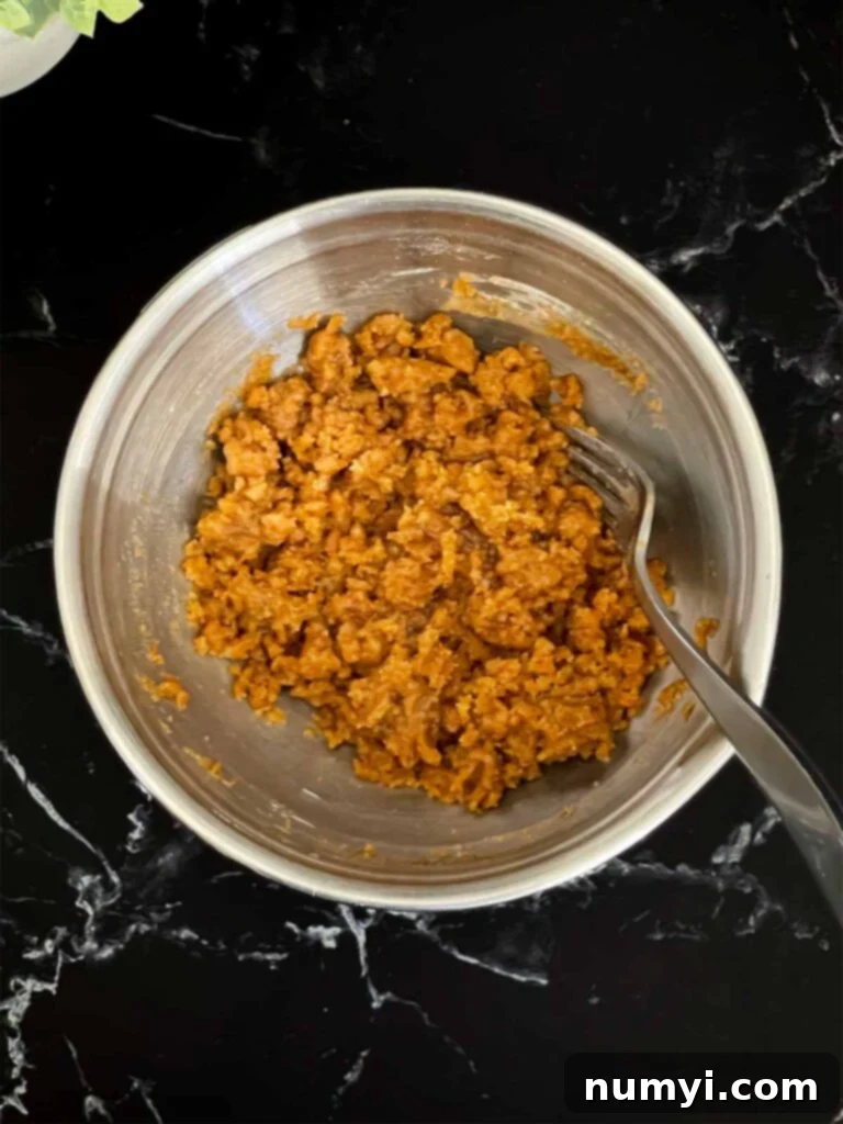 Streusel topping ingredients for carrot coffee cake mixed in a metal bowl on a dark surface, ready for the freezer.