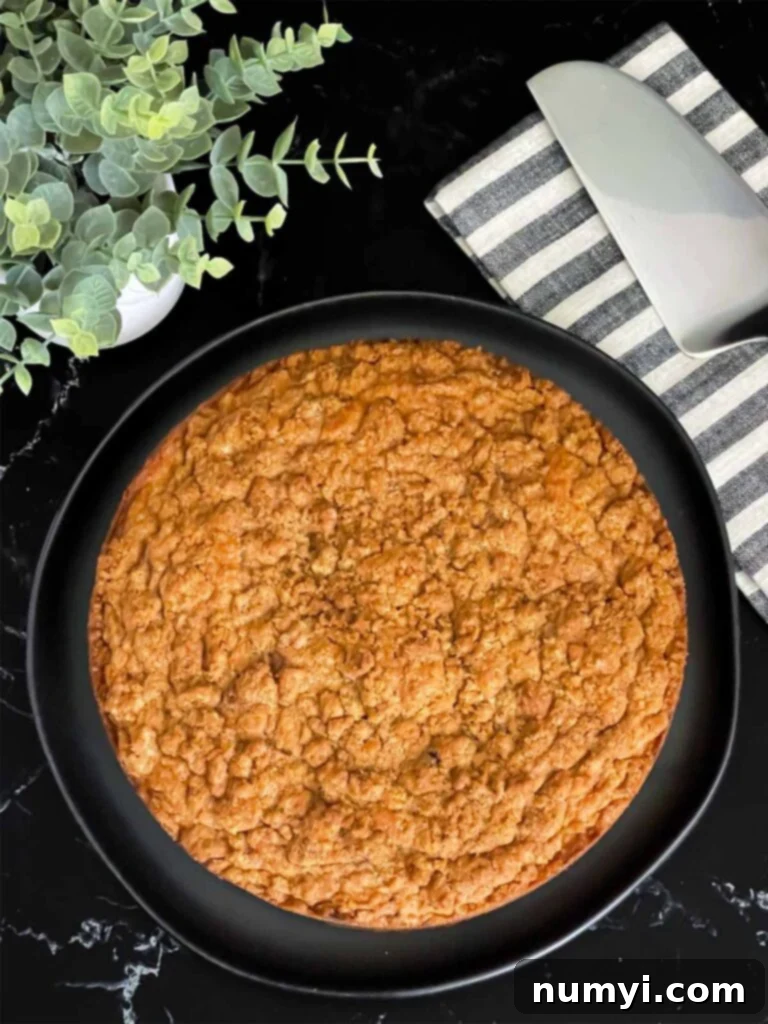 A freshly baked carrot coffee cake, golden brown with a crispy streusel topping, resting on a dark platter.