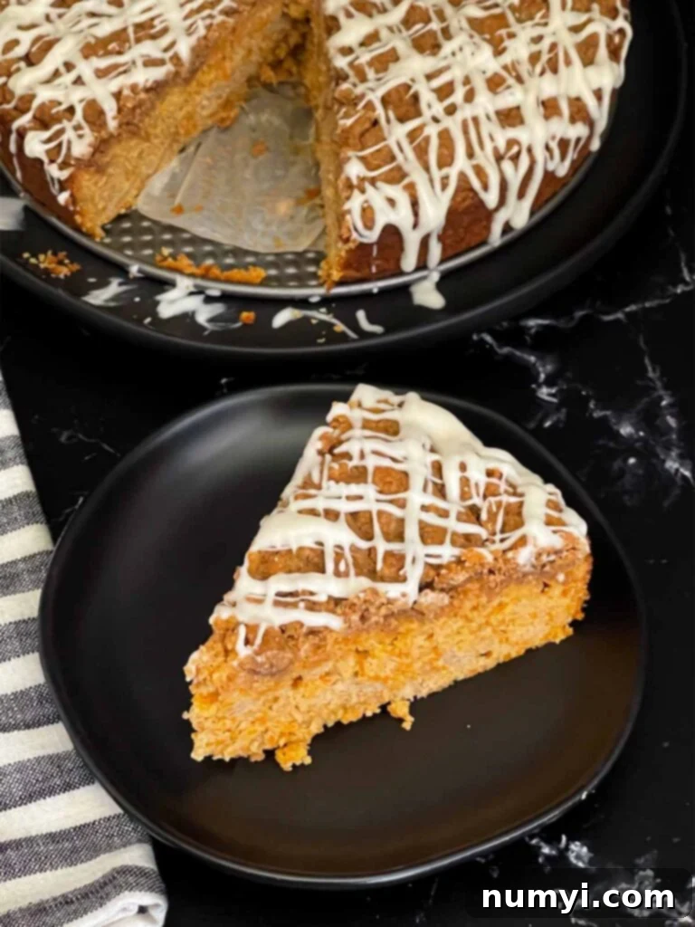 A slice of carrot coffee cake on a dark plate, showing its moist texture, streusel, and glaze, ready to be enjoyed.