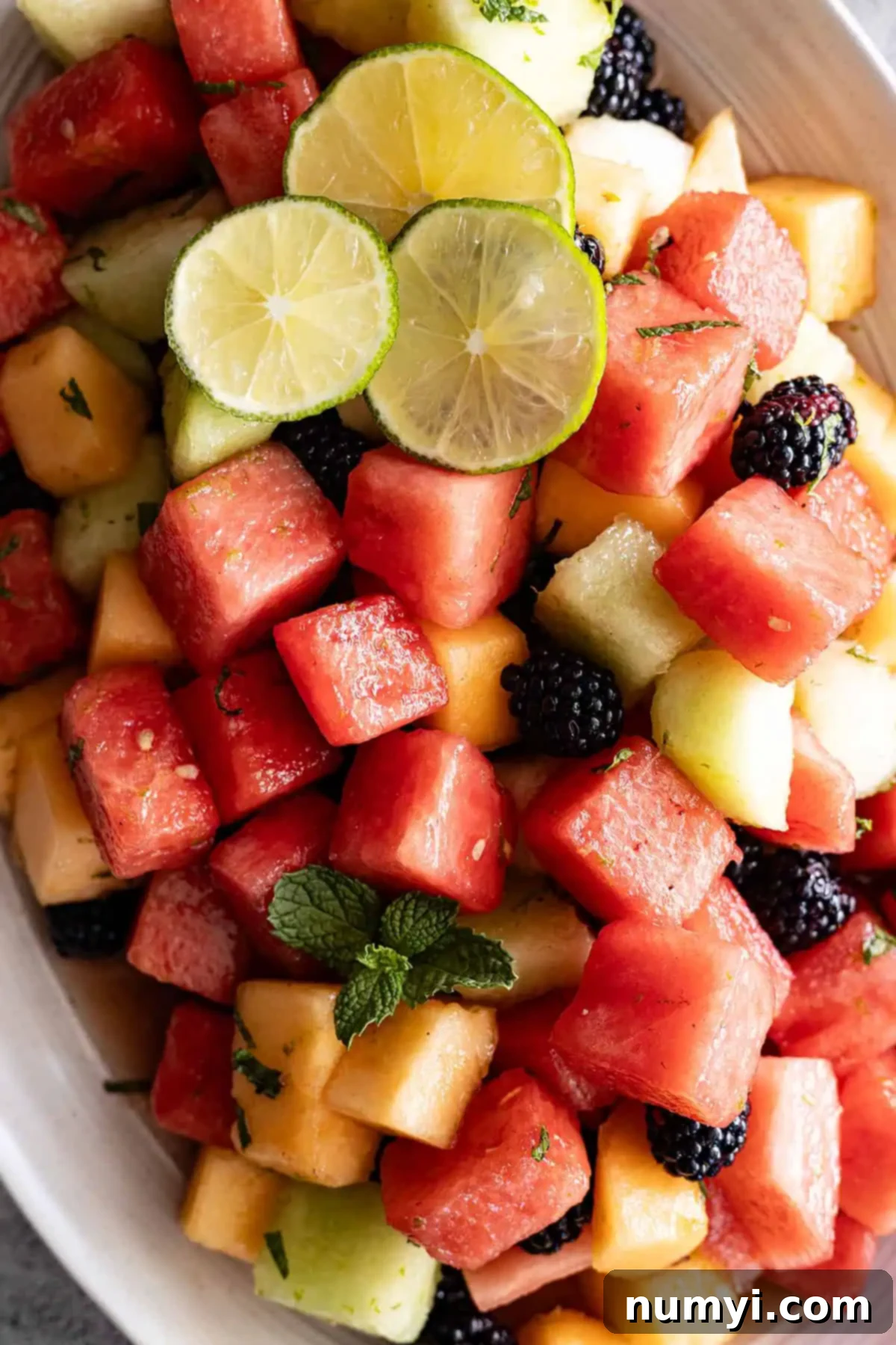 Overhead view of Mojito Fruit Salad served on a cream colored serving platter, garnished with lime wedges and fresh mint.