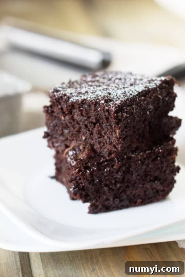 Two squares of incredibly fudgy zucchini brownies, stacked enticingly on top of each other, showcasing their moist texture.