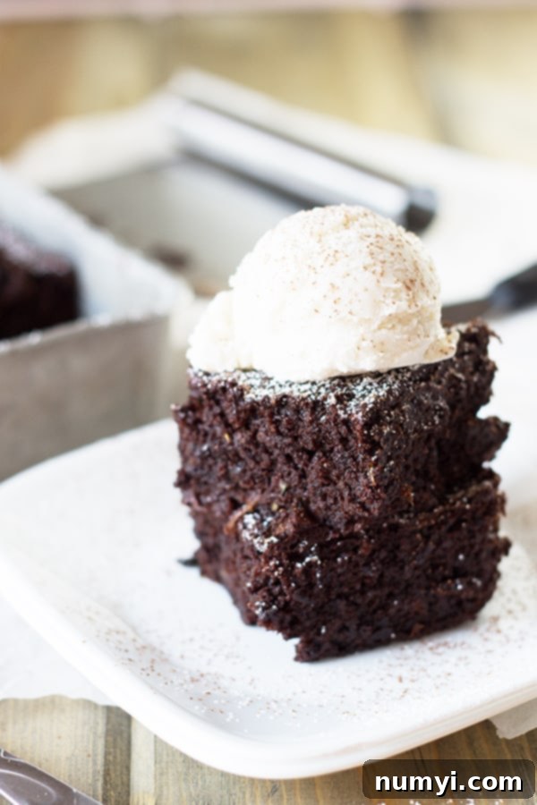 Two squares of rich, fudgy zucchini brownies, stacked with a dollop of creamy vanilla ice cream on top, ready for a dessert experience.