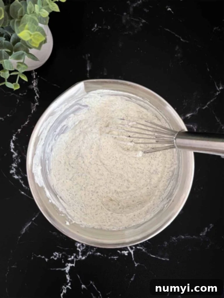 Dill dip whisked together in a metal bowl on a dark surface.