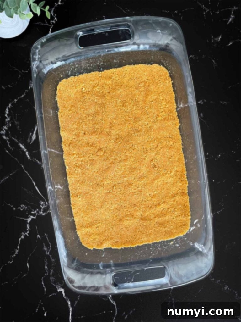 Lush Coconut Cream 4 Graham cracker crust for the coconut cream lush pressed into a 9x13 glass baking pan on a dark surface.