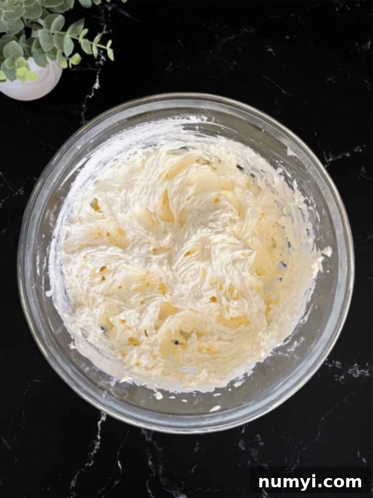 Lush Coconut Cream 6 Whipped topping mixed into the cheesecake mixture in a glass mixing bowl on a dark surface.
