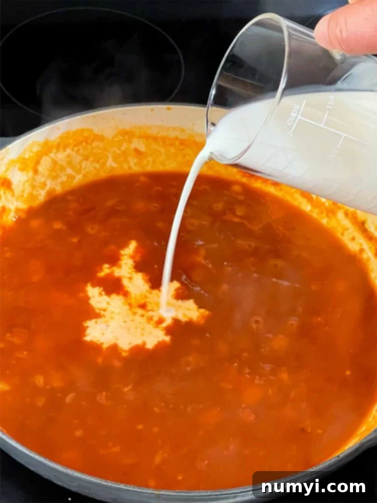 Adding cream to Vodka sauce cooking in a skillet.