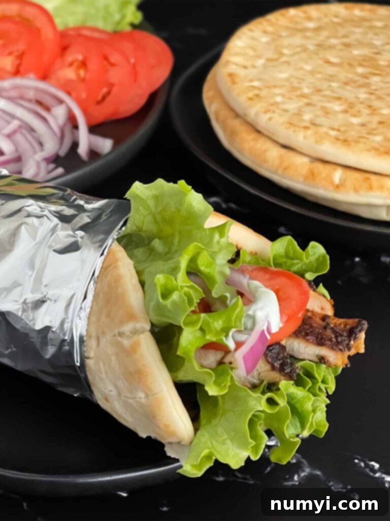 A perfectly assembled grilled chicken shawarma pita, filled with chicken, vegetables, and tzatziki sauce, on a dark plate.