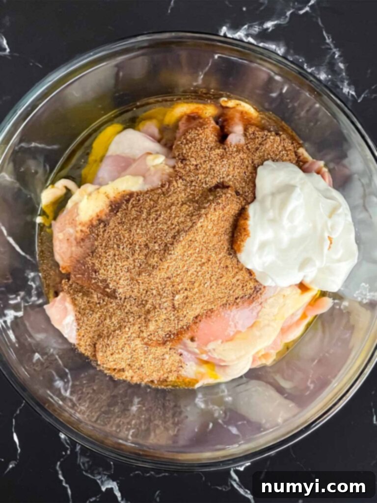 Marinated chicken thighs being added to a large bowl filled with shawarma marinade.