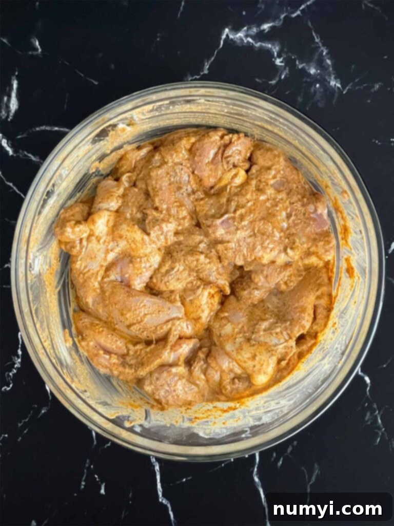 A bowl of chicken thighs thoroughly coated in a rich, aromatic shawarma marinade, ready for refrigeration.