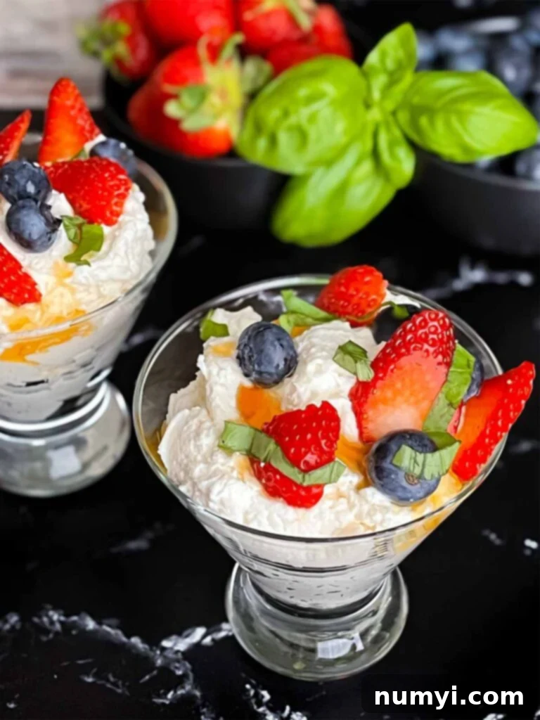 Ricotta mousse in a stemless martini glass garnished with strawberries, blueberries, basil, and honey.