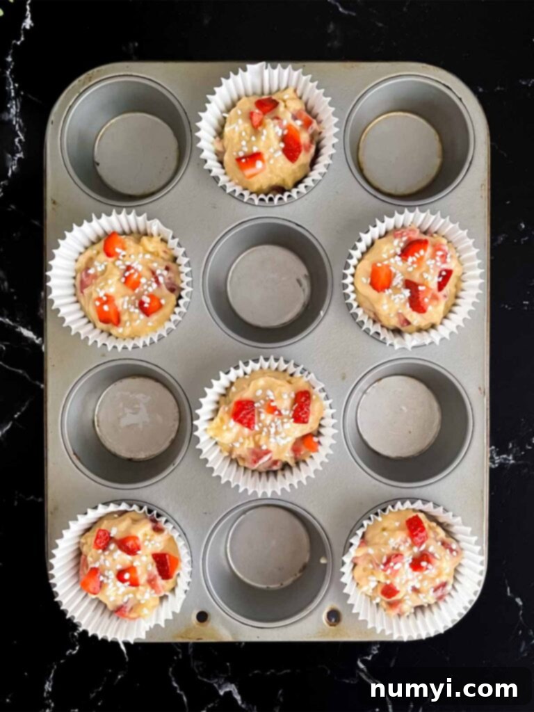 Strawberry muffin batter divided into six paper-lined muffin cups and sprinkled with pearl sugar, ready for baking.