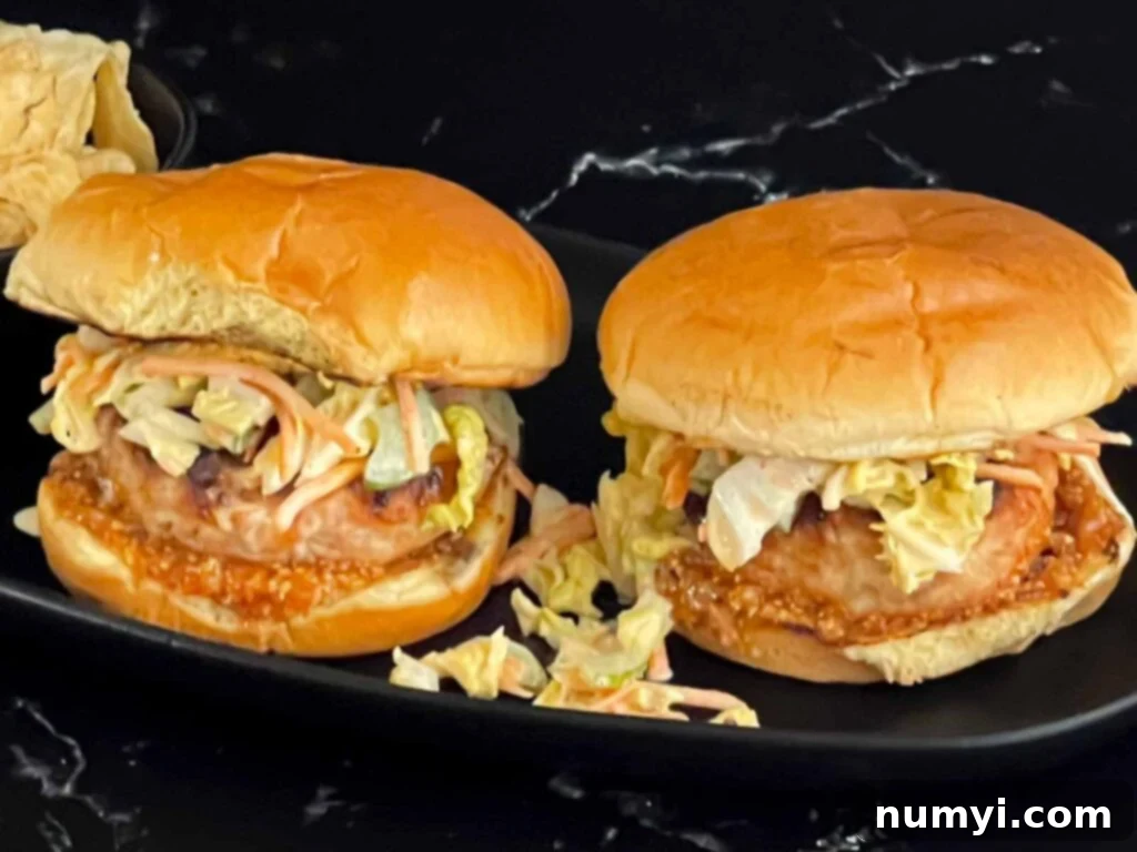 Zesty Carolina Grilled Chicken Burgers 2 Grilled Carolina chicken burgers on a black plate, topped with tangy sauce and crunchy slaw.