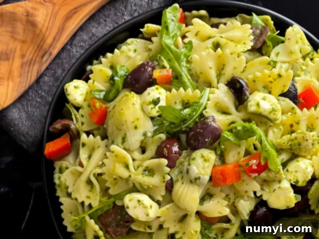Mediterranean pasta salad in a dark bowl on a dark surface, garnished with fresh herbs.