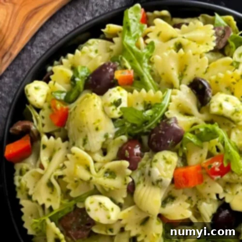 Mediterranean pasta salad in a dark bowl on a dark surface, ready to be served.