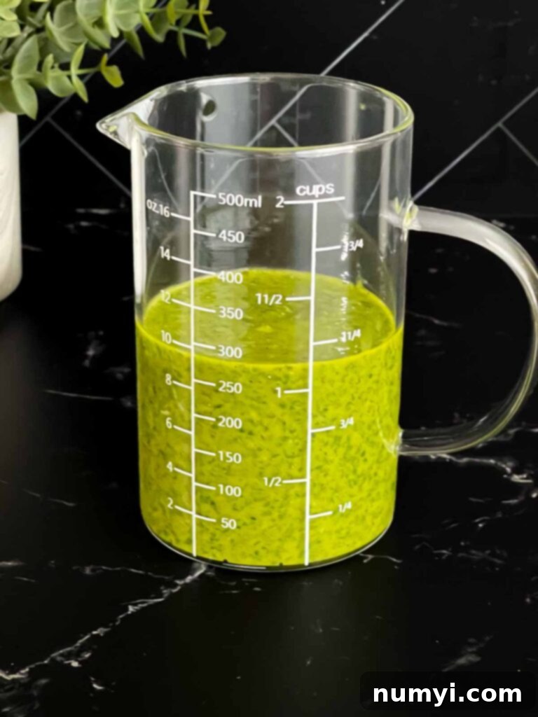 The emulsified fresh herb vinaigrette in a clear glass measuring cup, ready to be used.
