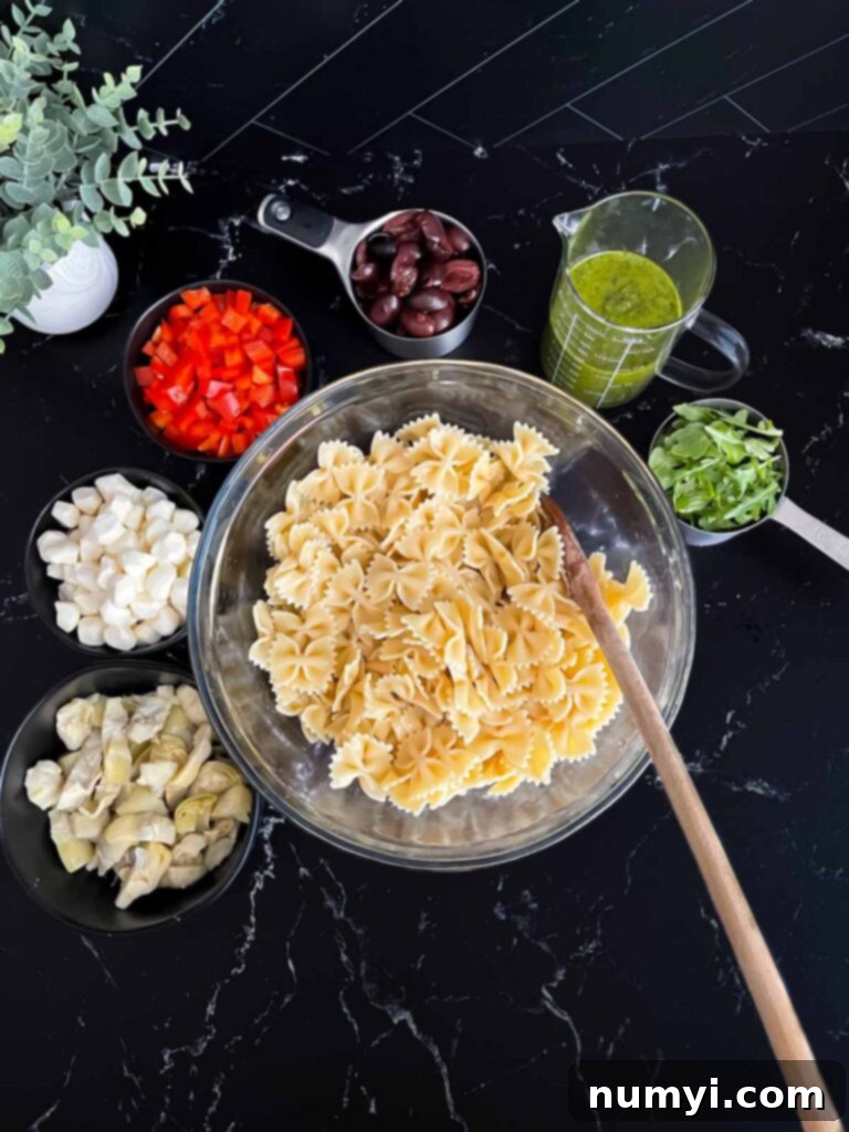 Cooked Farfalle pasta in a glass bowl, surrounded by prepped salad ingredients like olives, bell peppers, and cheese.
