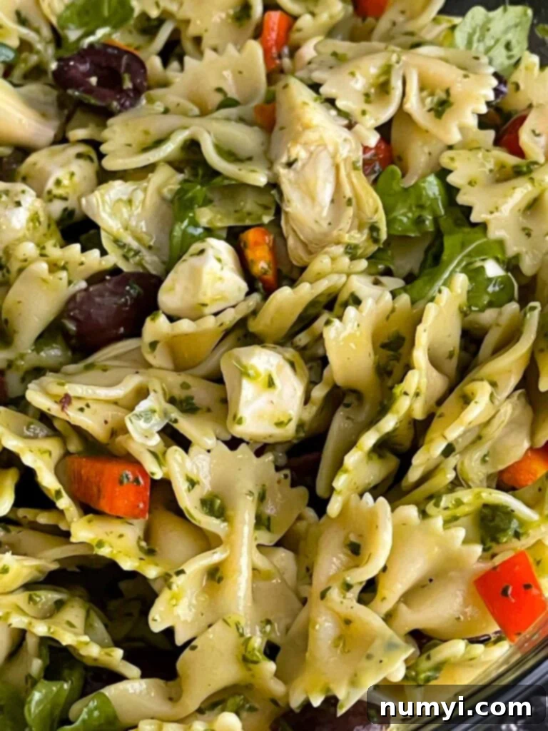 Mediterranean pasta salad mixed and ready to serve in a clear glass bowl, showcasing the colorful ingredients.