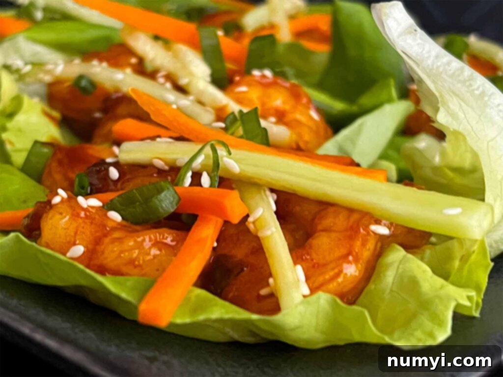 Two Gochujang shrimp lettuce wraps ready to be eaten, showcasing the fresh ingredients and the vibrant red shrimp.