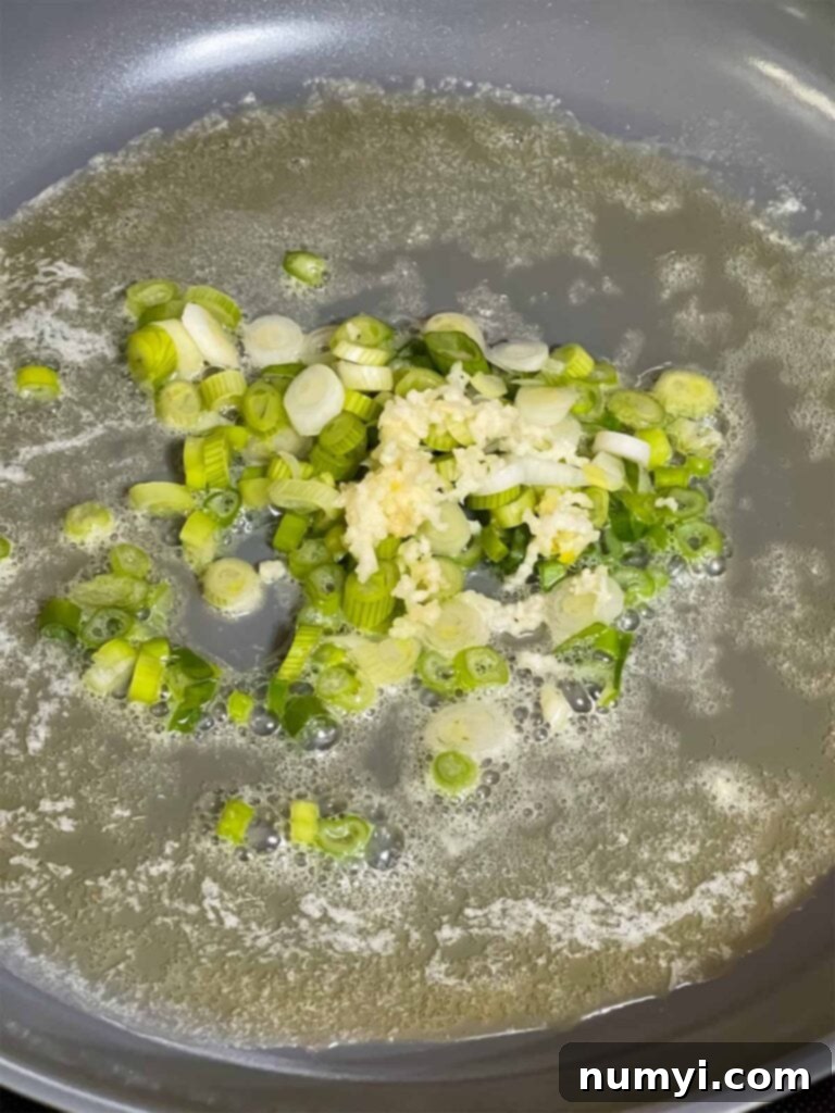 Sliced white parts of green onions and minced garlic sizzling gently in melted butter and sesame oil in a hot skillet.