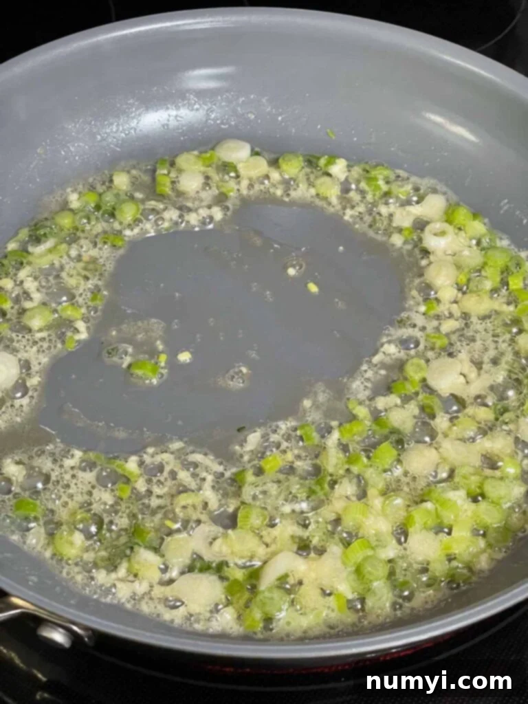 Close-up of sautéed garlic and thinly sliced green onion in a skillet, softened and fragrant.