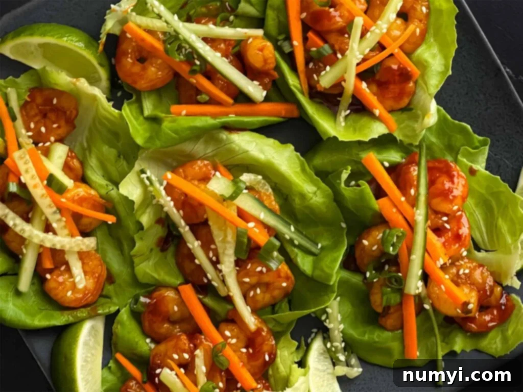 Gochujang shrimp lettuce wraps arranged beautifully on a white platter, garnished with fresh herbs and lime wedges.