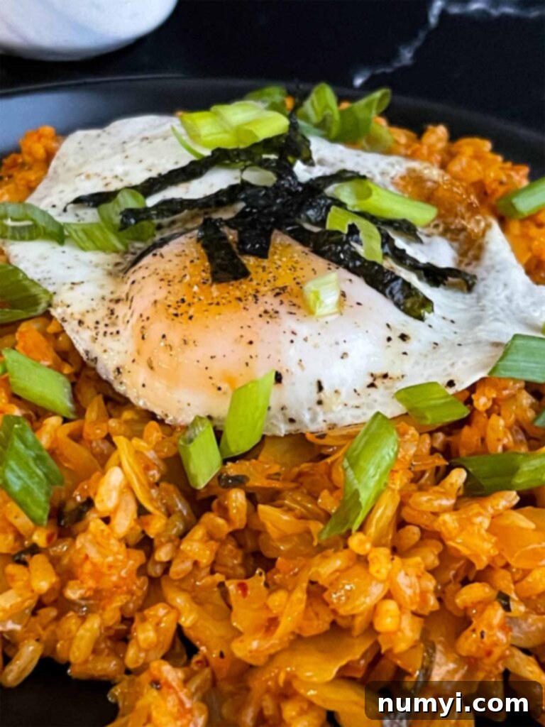 A close-up view of kimchi fried rice, showing the vibrant colors and textures, garnished with green onions and gim.