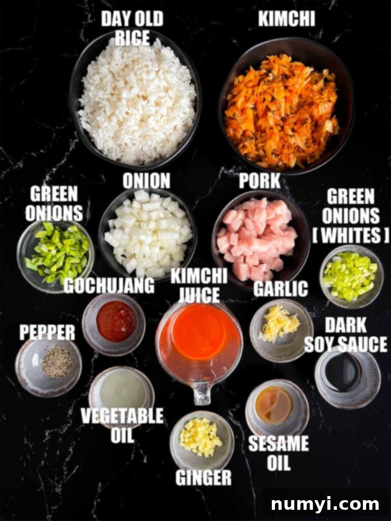 A collection of fresh ingredients laid out on a cutting board, including diced pork, kimchi, rice, onions, garlic, ginger, and green onions, ready for making kimchi fried rice.