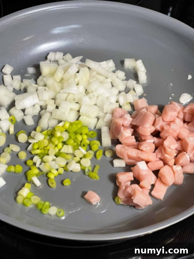 Diced onions, the white parts of green onions, and diced pork sizzling in a hot skillet, beginning to cook.
