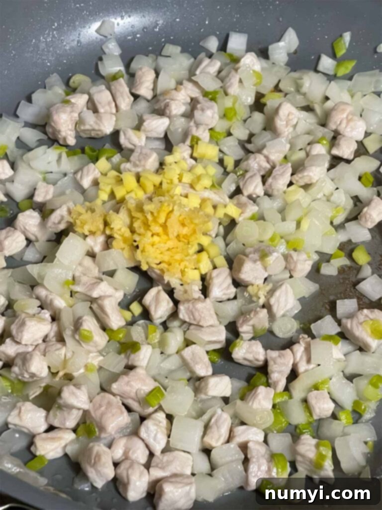 Onions, green onions, pork, minced ginger, and minced garlic cooking together in a skillet, creating aromatic flavors.