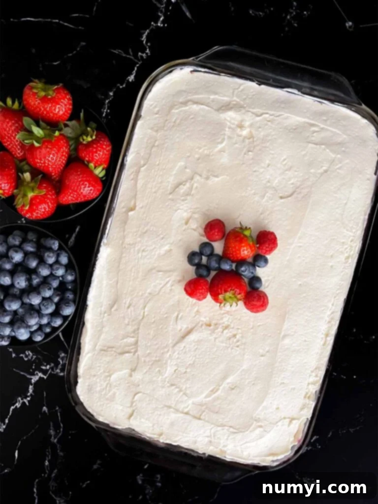 Luscious Berry Poke Cake 13 The finished Berry Poke Cake, generously covered with fluffy whipped cream cheese frosting and beautifully garnished with fresh strawberries, raspberries, and blueberries.