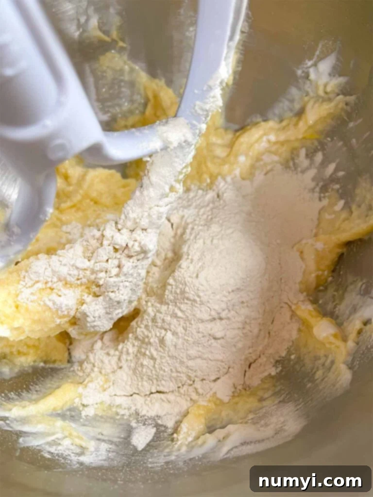 Luscious Berry Poke Cake 6 All-purpose flour being gently added to the creamed ingredients, alternating with buttermilk, for the berry poke cake recipe.