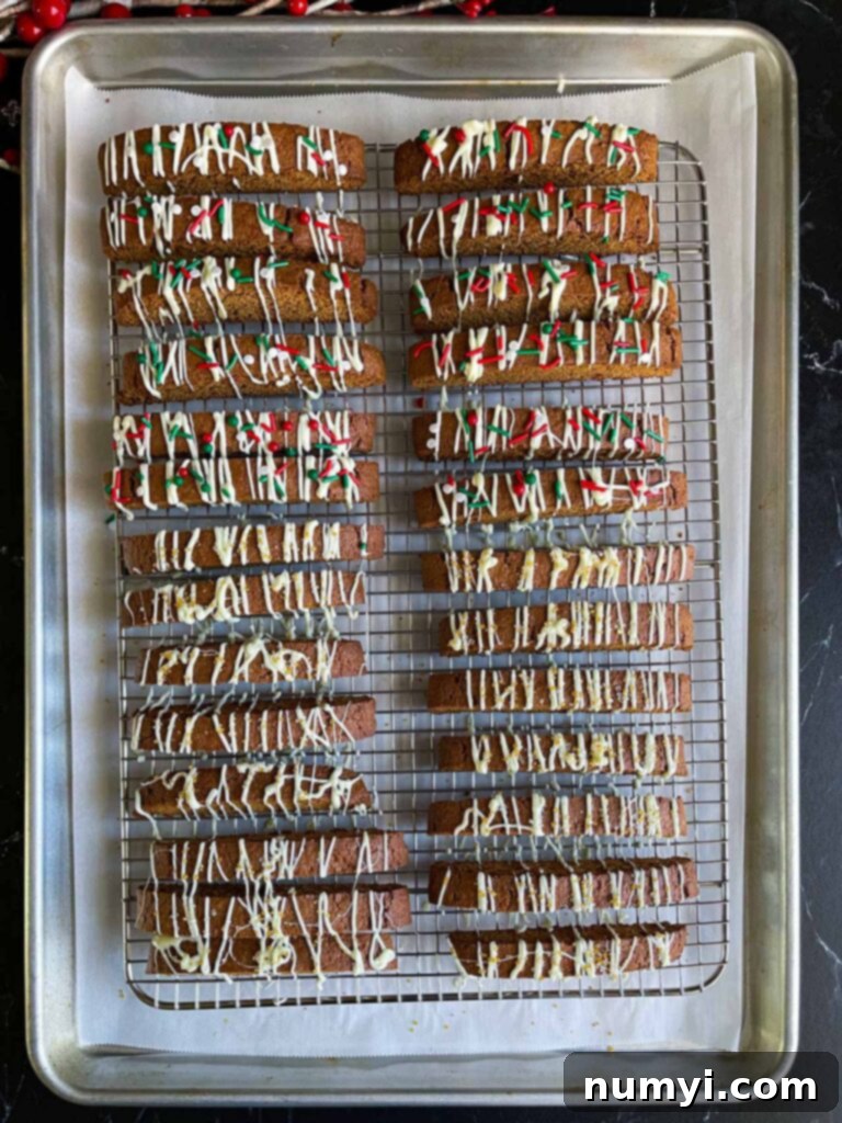 Gingerbread biscotti on a wire rack in a baking sheet drizzled with white chocolate and sprinkles.