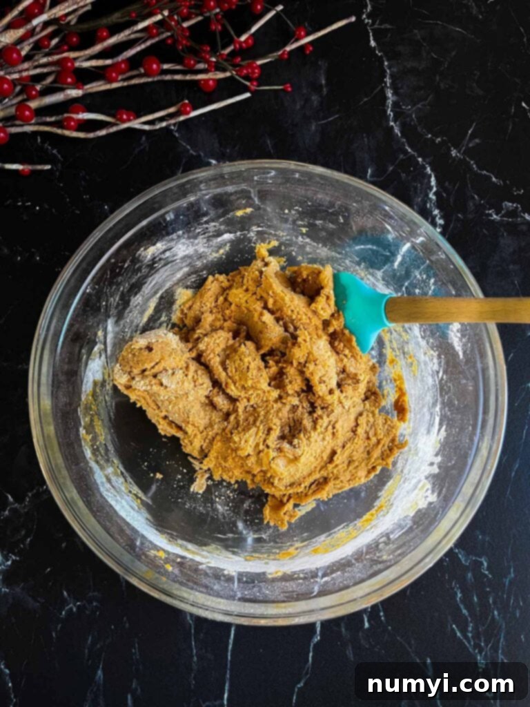 Gingerbread biscotti dough in a glass mixing bowl on a dark background.