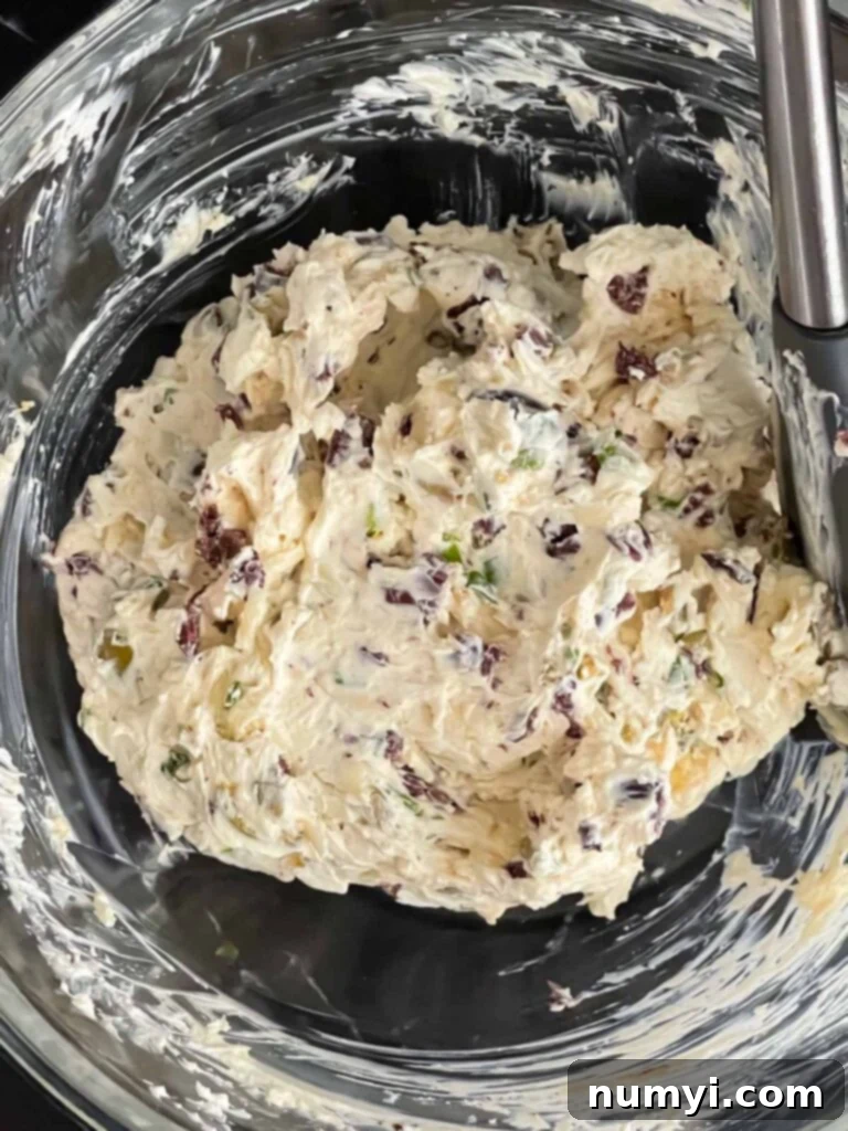 Olive cheese ball ingredients blended together in a glass mixing bowl.