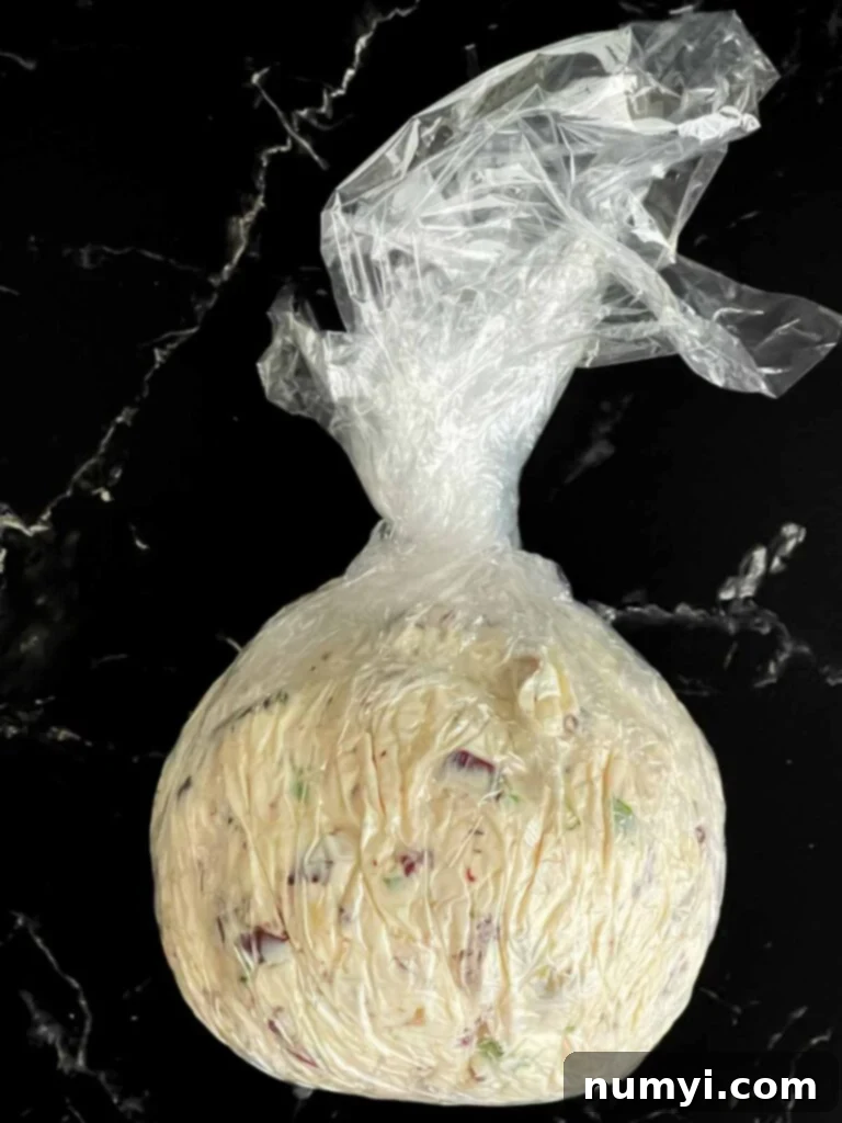 Olive cheese ball formed in plastic wrap on a dark surface.