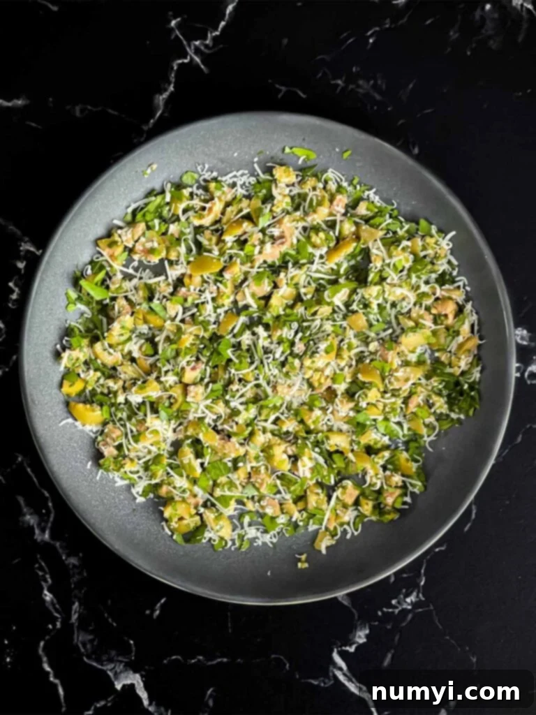 Olive cheese ball coating ingredients mixed in a shallow bowl on a dark surface.