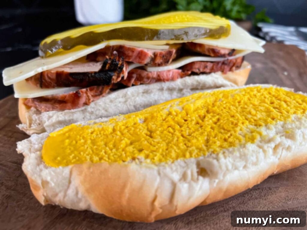 Assembling a grilled Cuban pork tenderloin sandwich with multiple layers of meat and cheese.