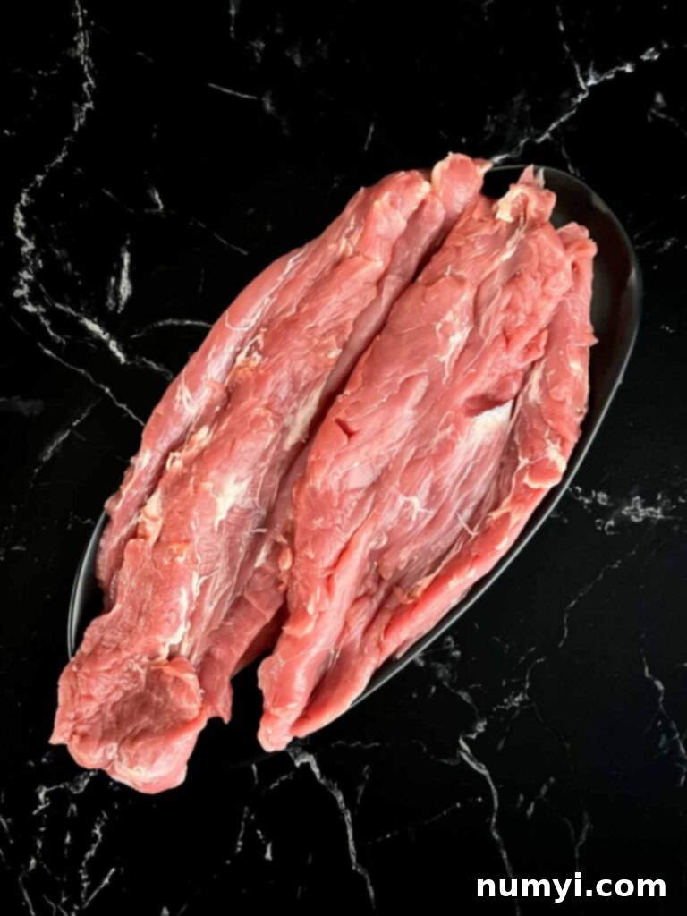 Roll-cut pork tenderloin on a black cutting board, partially opened.