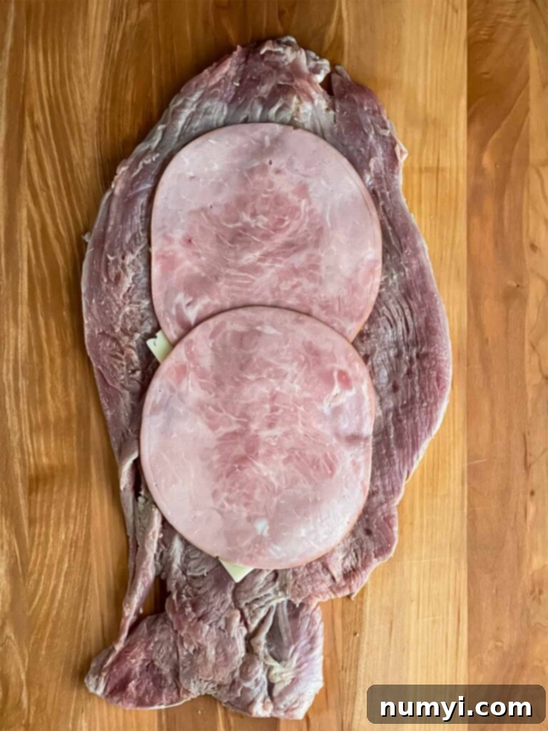 Deli ham and Swiss cheese layered onto a flattened pork tenderloin, ready for rolling.