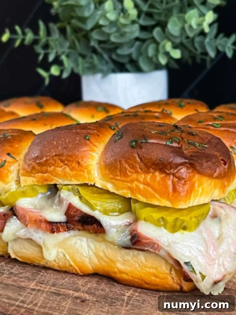 Oven-baked roll-cut pork tenderloin Cuban sliders, with golden brown tops and melted cheese visible.