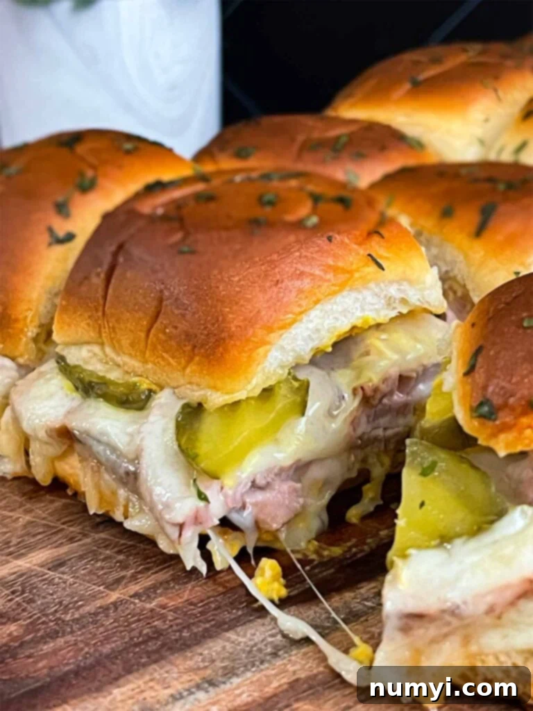 A close-up of a pan of golden brown, melty roll-cut pork tenderloin Cuban sliders fresh from the oven.