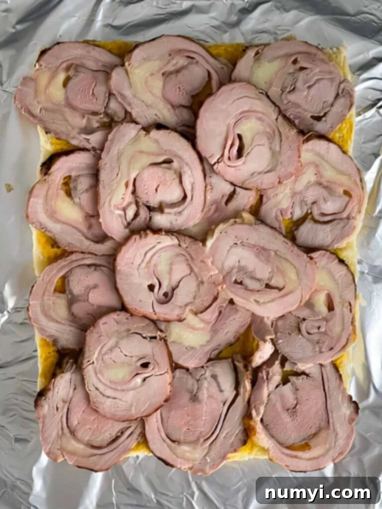 Thinly sliced grilled pork tenderloin roulade being layered onto the bottom halves of slider rolls.
