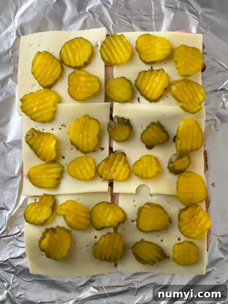 Crisp dill pickles being added as the final layer on top of the cheese for the pork tenderloin sliders.
