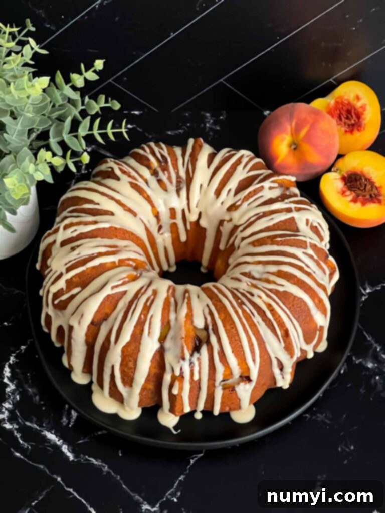 A glorious peach pound cake, perfectly glazed, on a dark plate on a dark surface.