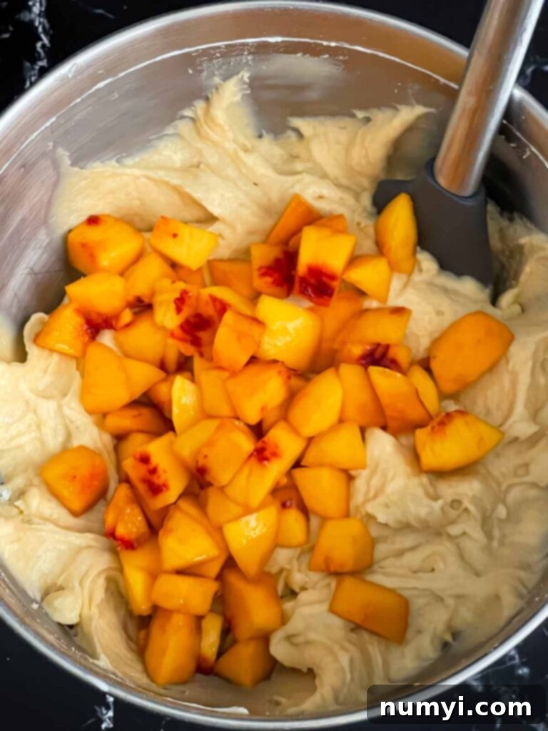 Peach chunks added to the peach pound cake batter in a metal mixing bowl.