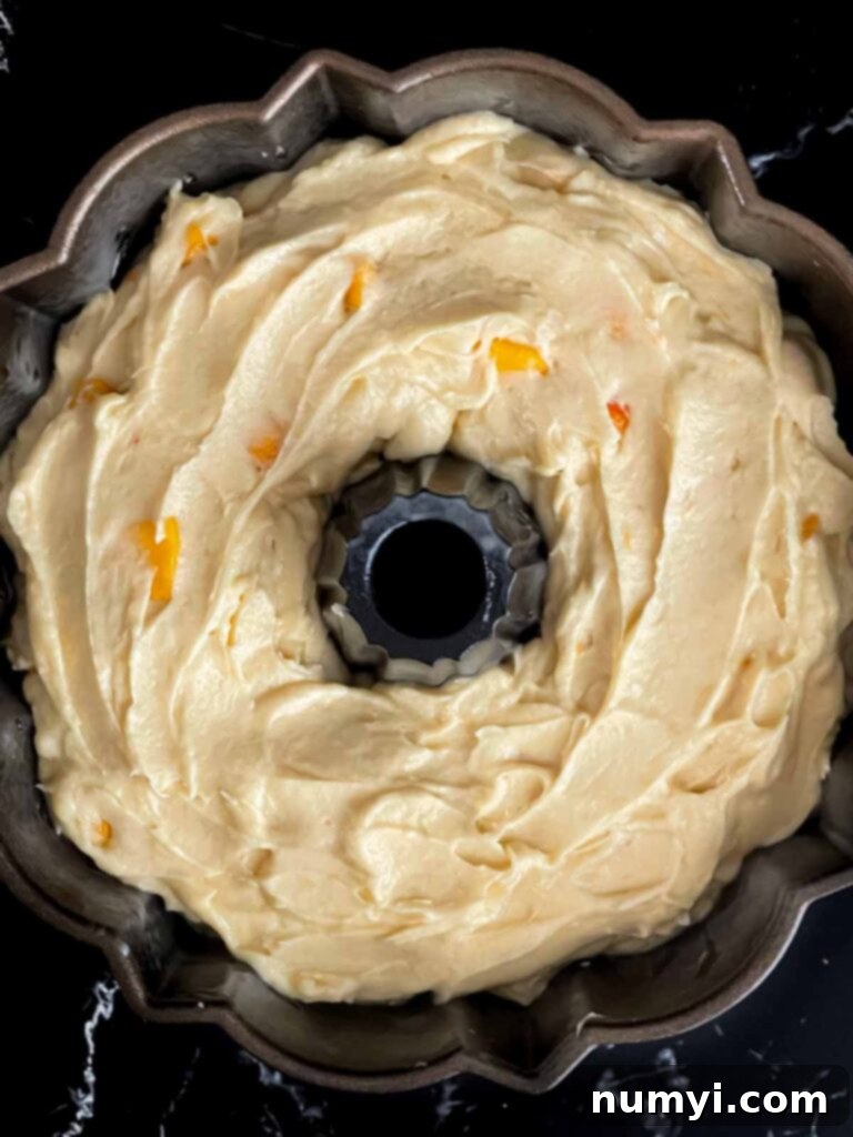 Peach pound cake batter in a bundt pan on a dark surface, ready for baking.