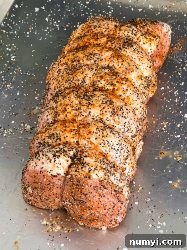 A pork loin trussed and seasoned with salt and black pepper on a baking sheet, ready for the smoker.