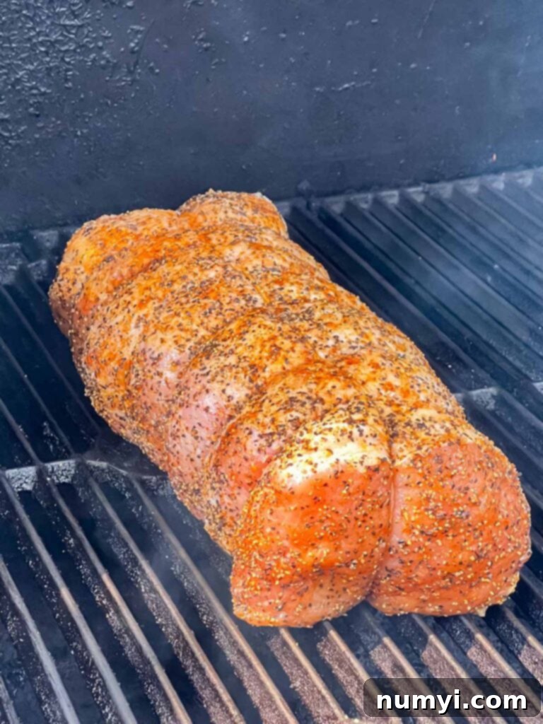 A pork loin being placed on a smoker rack.